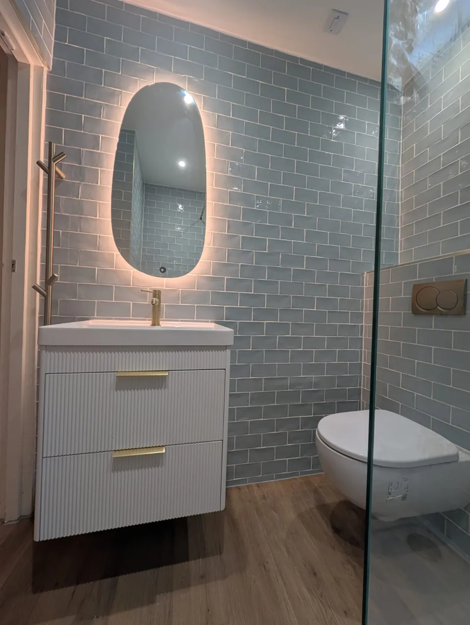 Compact vanity and illuminated mirror against blue tiles