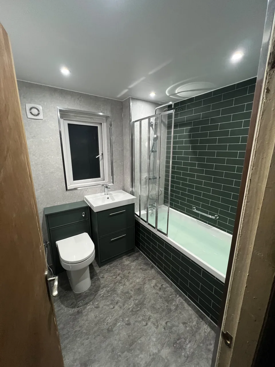 Green-tiled bath with shower screen and fitted storage